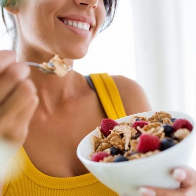 Portrait of beautiful young woman eating cereals and fruits at home.